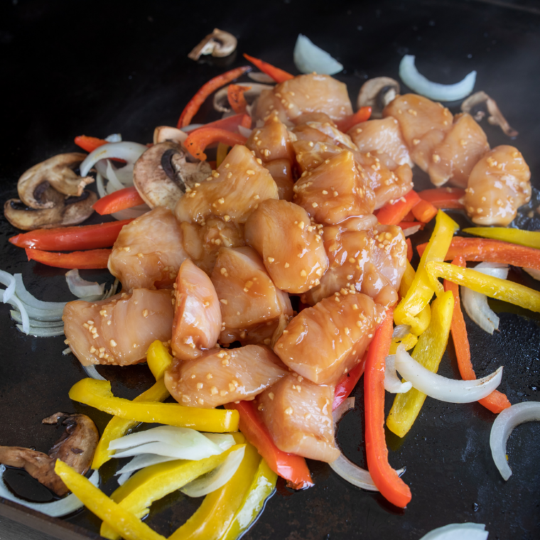 Diced onion, red bell pepper, and chipotle cooking with chicken on the Blackstone griddle.