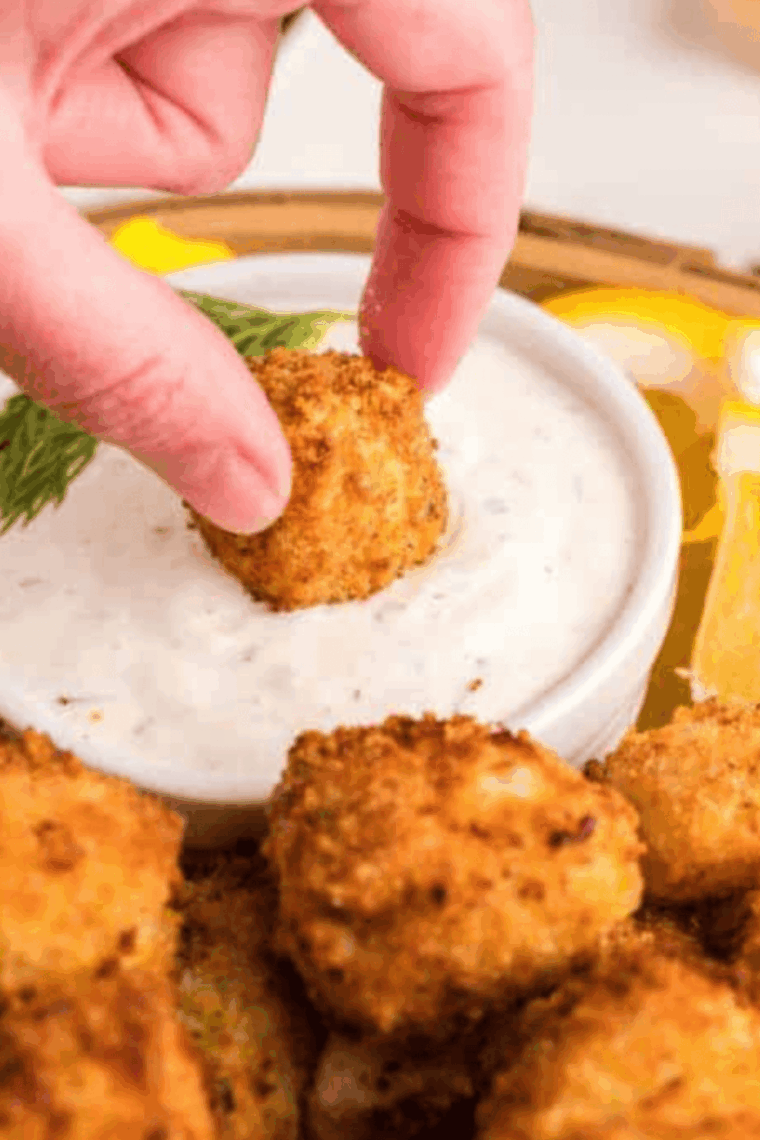 Plate of crispy golden-brown fried catfish nuggets with a side of tartar sauce and lemon wedges.
