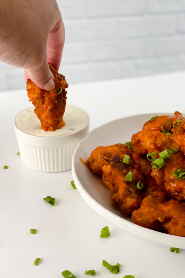 Golden-brown air fryer chicken tenders coated in buffalo sauce, served with celery sticks and a small bowl of dipping sauce.