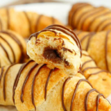 Air fryer peanut butter chocolate crescent rolls stacked on a white plate with chocolate drizzle