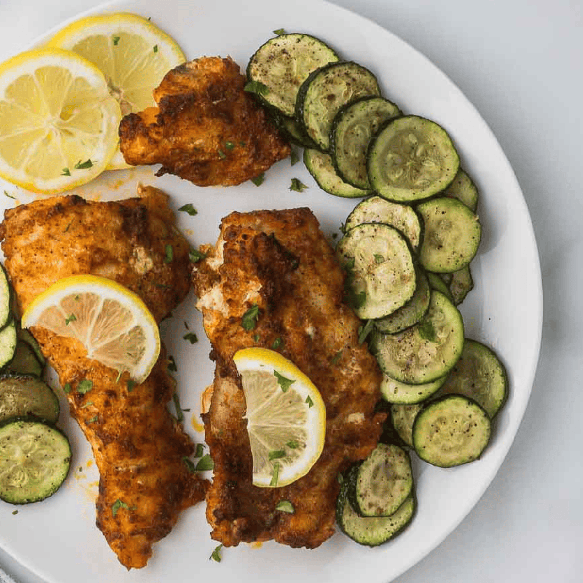Golden crispy air fryer zucchini slices seasoned with zaatar spice on a white plate.