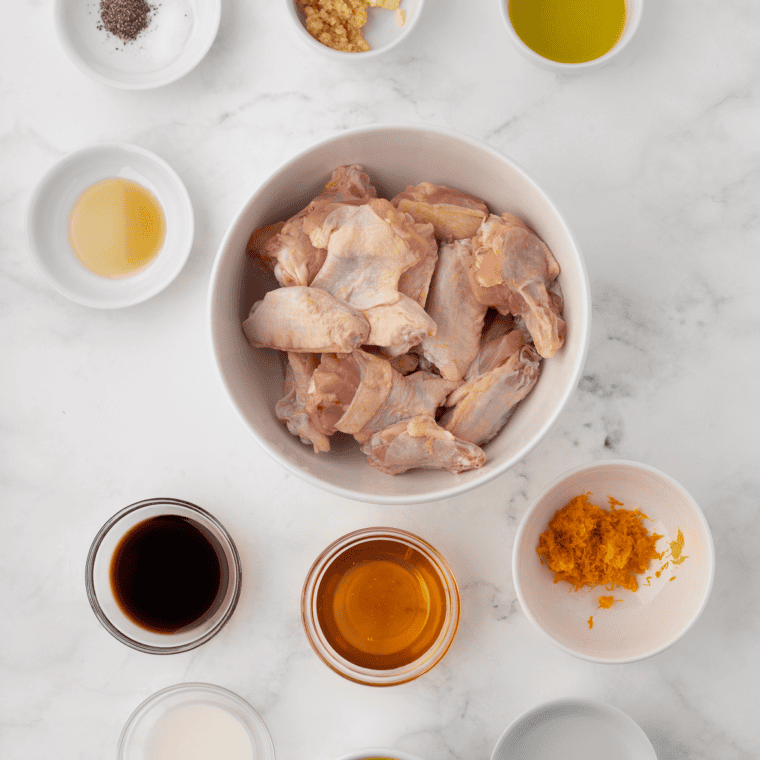 Ingredients for copycat Hooters lemon pepper wings, including raw chicken wings, baking powder, lemon zest, coarse black pepper, garlic powder, and melted butter