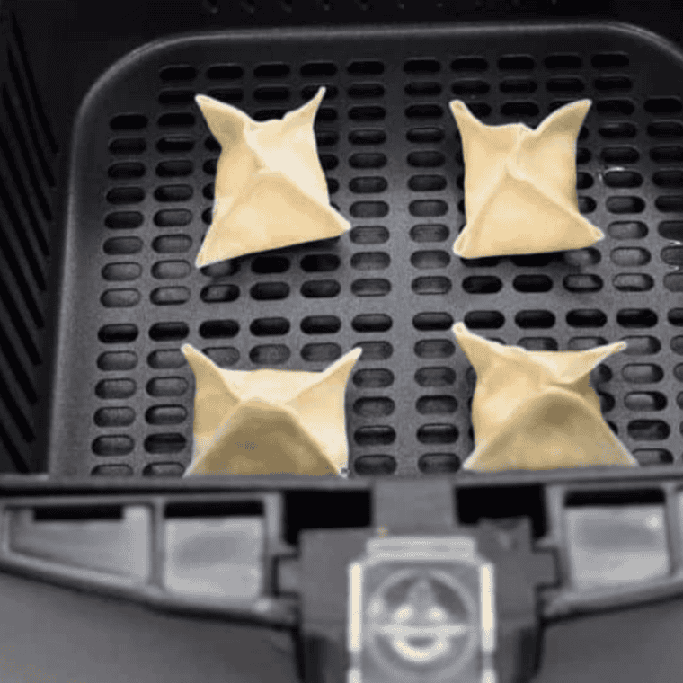 Crab rangoon reheating in an air fryer basket, turning golden brown and crispy with visible crunchy wonton edges and creamy filling inside.