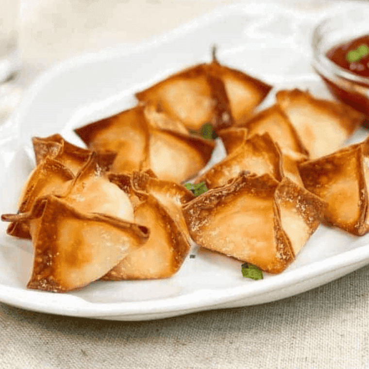 Crab rangoon pieces crisping in an air fryer basket, golden brown with crunchy edges and creamy filling visible.