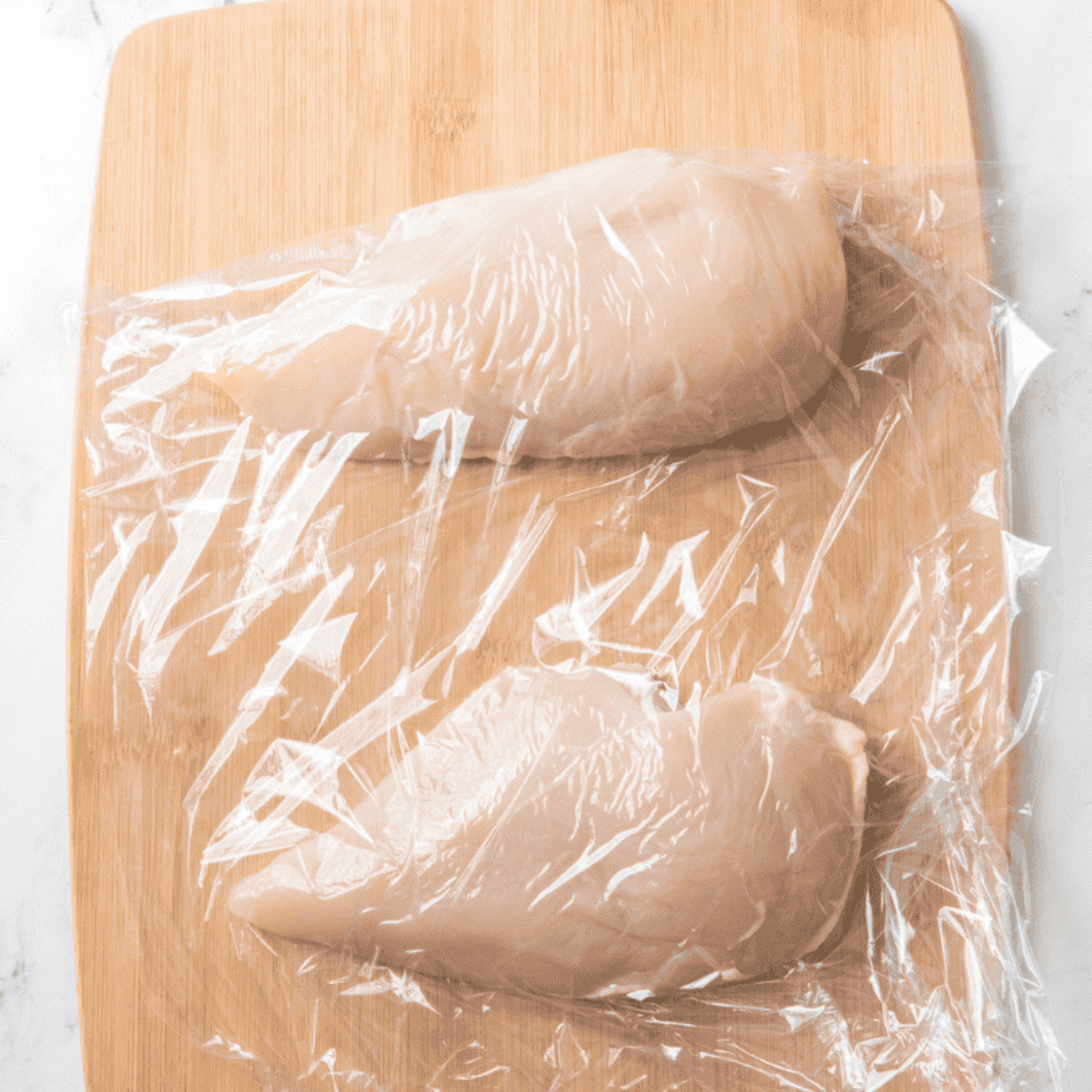 Flattening chicken with a meat mallet before air frying preparation.