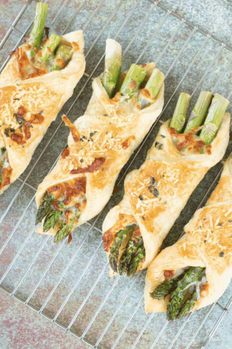 Golden puff pastry bundles filled with tender asparagus spears and melted cheese, cooked in the air fryer and served on a white plate.