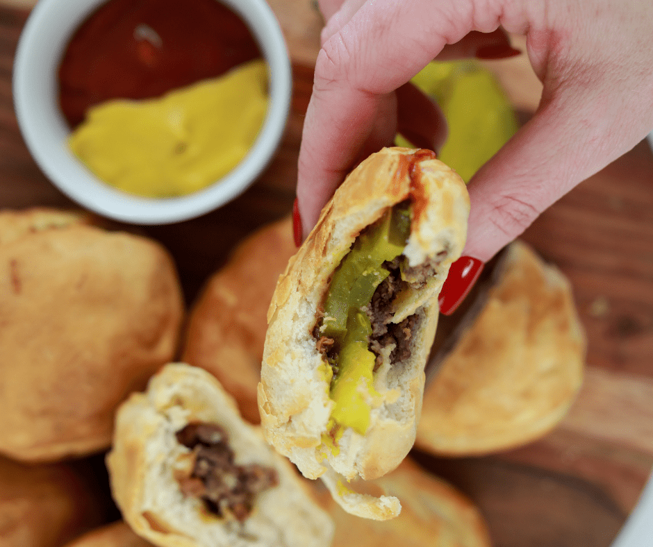 overhead: a hand holding an air fryer cheeseburger bacon bomb with a bite taken out of it