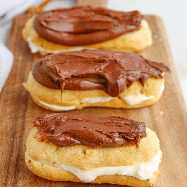 Golden air fryer eclairs filled with creamy custard and topped with a glossy chocolate glaze, served on a white plate.