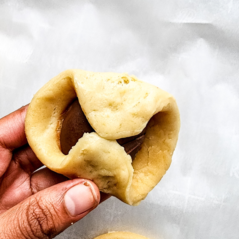 Pinch the seams of biscuit dough closed, place in air fryer basket, and brush with melted butter for golden, delicious Nutella Bombs.