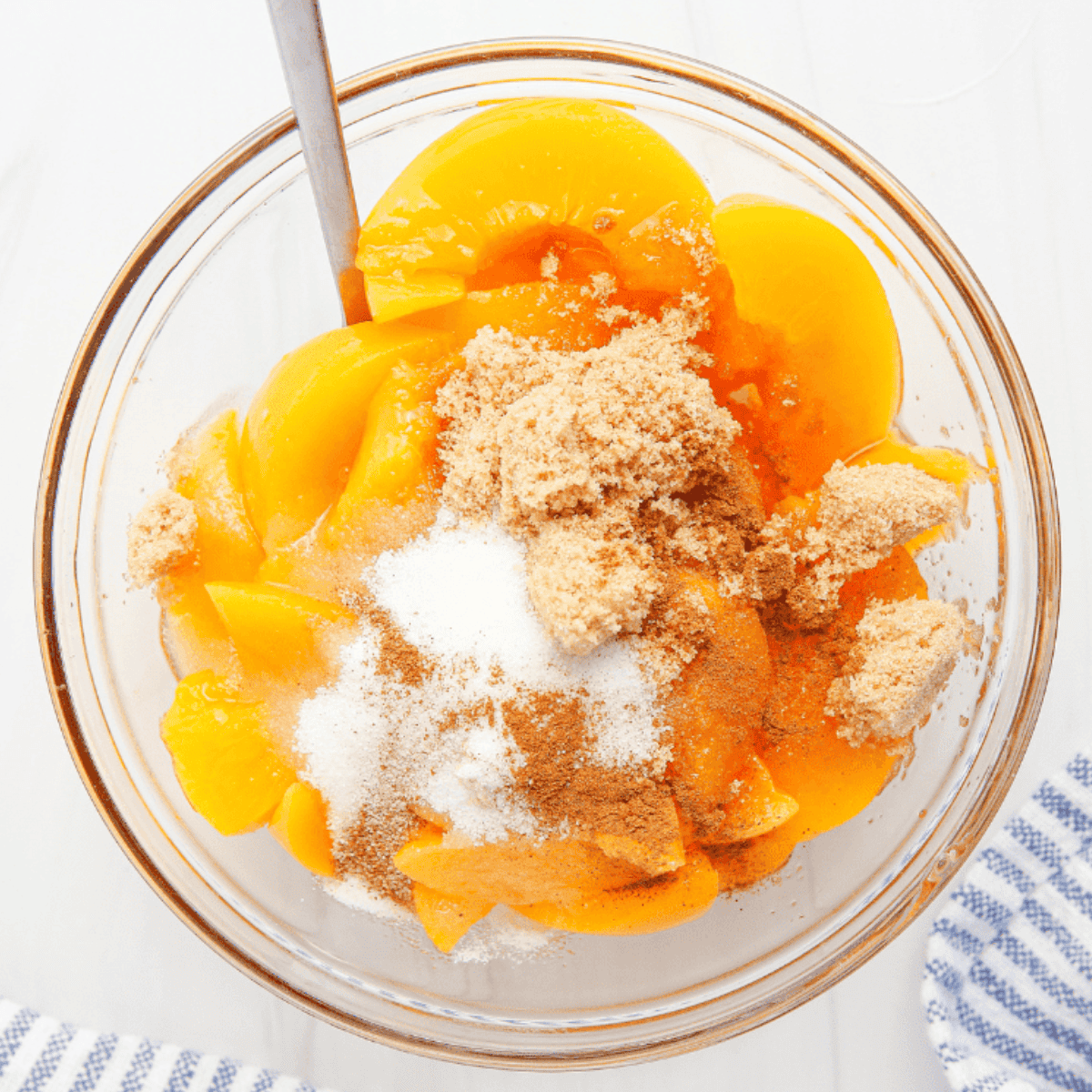 Sliced peaches in a mixing bowl coated with sugar, flour, and cinnamon.