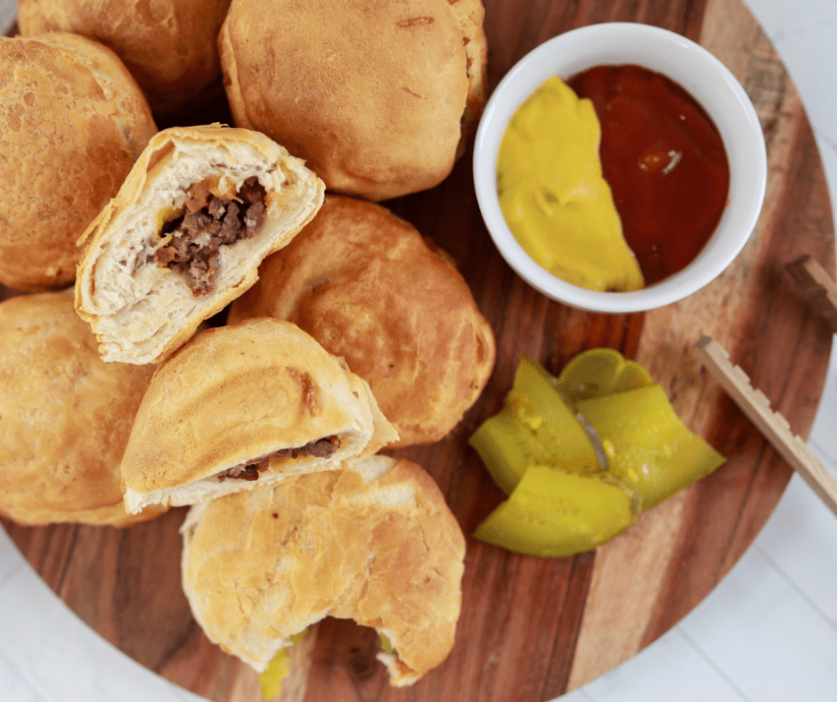 overhead: air fryer bacon cheeseburger bombs on a wooden board with ketchup, mustard, and pickles