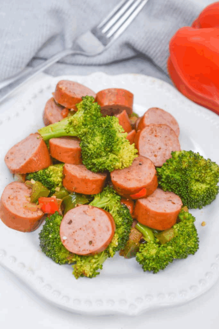 Golden sausage slices and roasted broccoli cooked in the air fryer, served hot on a white plate.
