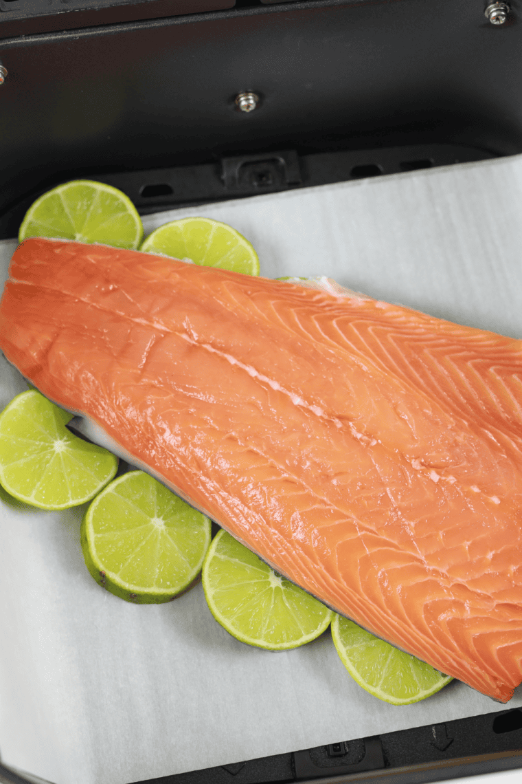 Salmon fillets placed on soaked cedar plank inside air fryer basket.