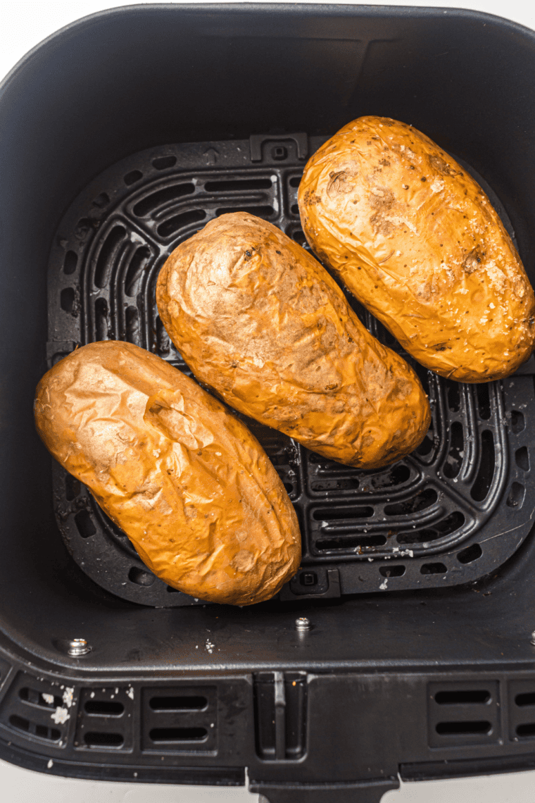 Air fryer steakhouse potatoes sliced open and topped with cheese, butter, and herbs.