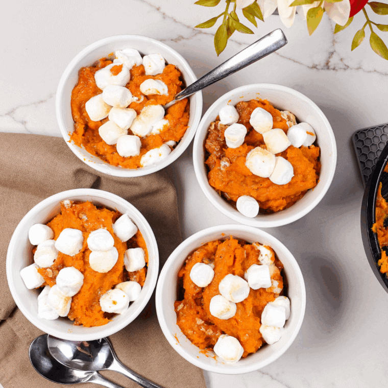 Baked sweet potato casserole made with canned yams and topped with golden, toasted marshmallows in a white dish.
