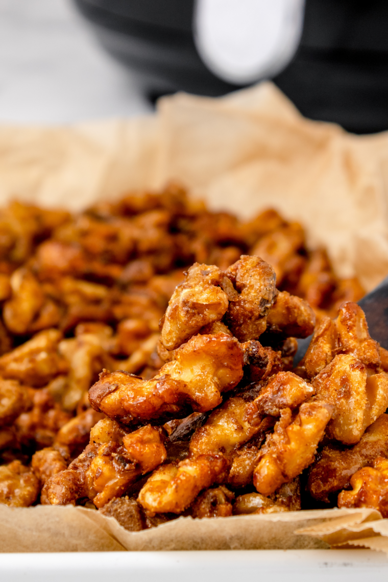 Bowl of air fryer honey roasted walnuts coated in a glossy cinnamon honey glaze.