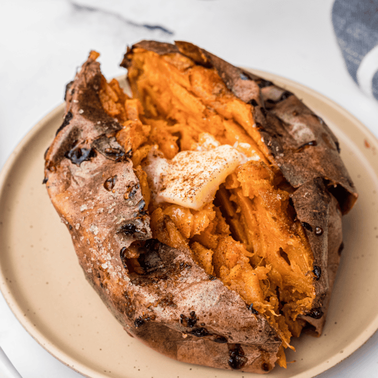 Close up of a reheated baked sweet potato with crackling crisp skin and soft orange flesh inside