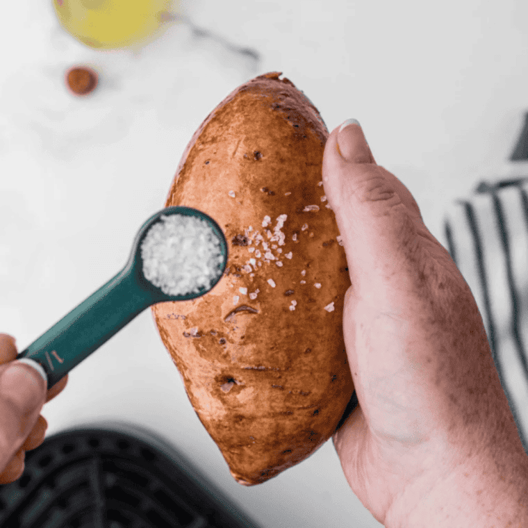 Hand rubbing olive oil onto a cold baked sweet potato with salt sprinkled over the dried skin