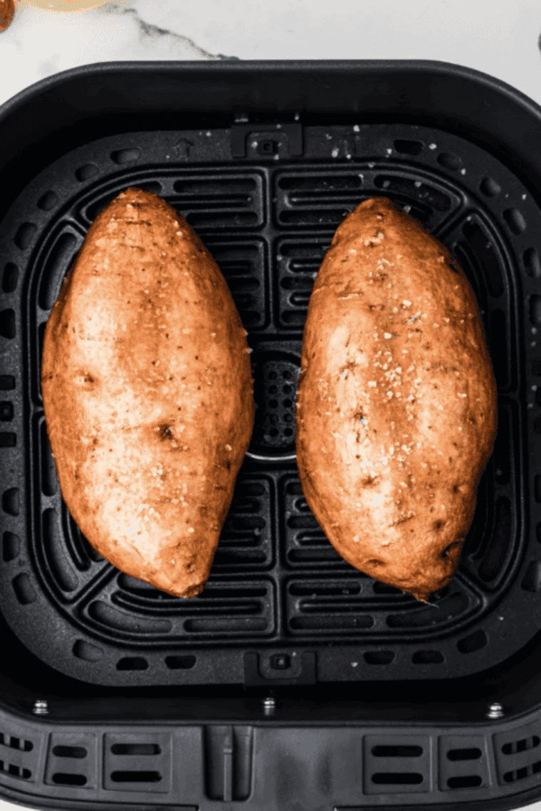 Two sweet potatoes placed directly in an air fryer basket with no foil, spaced apart in a single layer