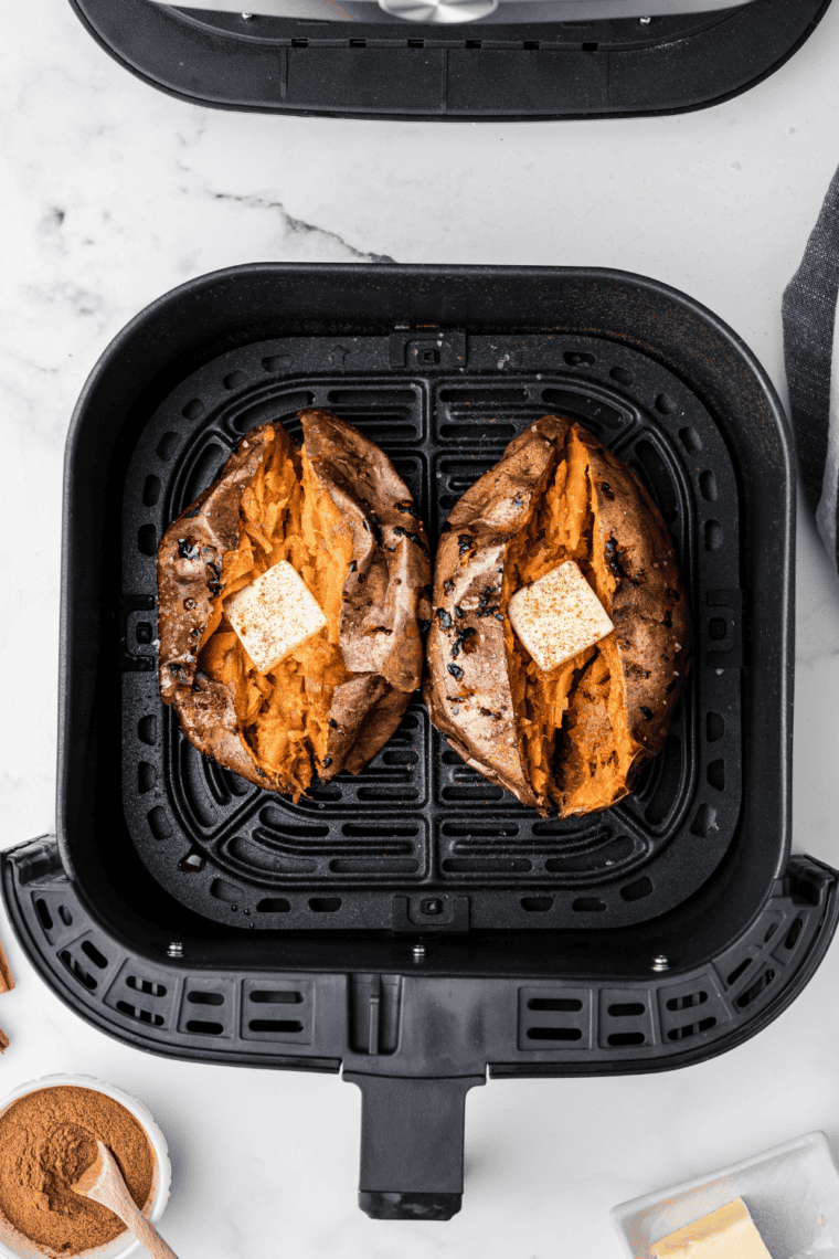 Reheated sweet potato split lengthwise with the flesh fluffed by a fork and a pat of butter melting on top