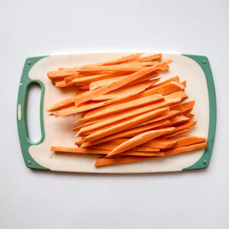 Peeling and cutting sweet potatoes into thin fries on a cutting board."