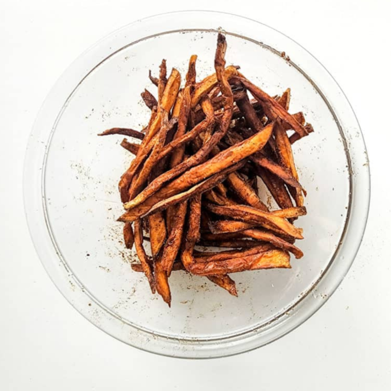 Mixing sweet potato fries with olive oil and spices in a bowl."