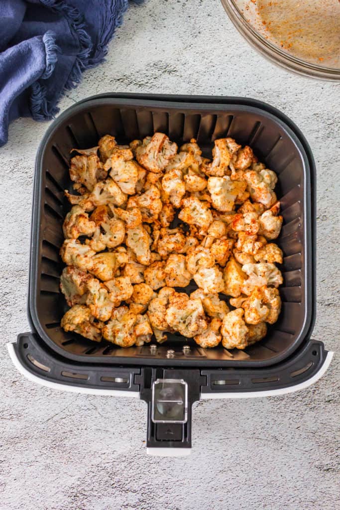 Image of marinated cauliflower pieces arranged on the air fryer basket.