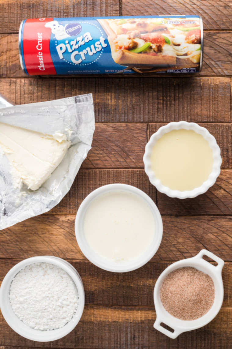 Overhead view of ingredients for Cinnastix: pizza dough, melted butter, granulated sugar, and cinnamon sugar on a countertop.