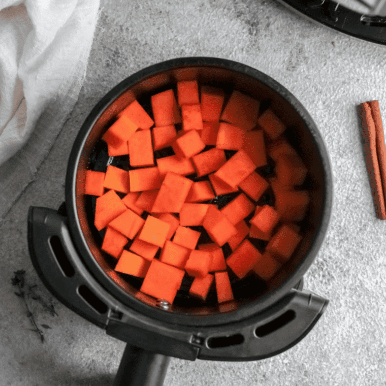 Seasoned pumpkin cubes in a single layer in the air fryer basket before roasting at 400&deg;F