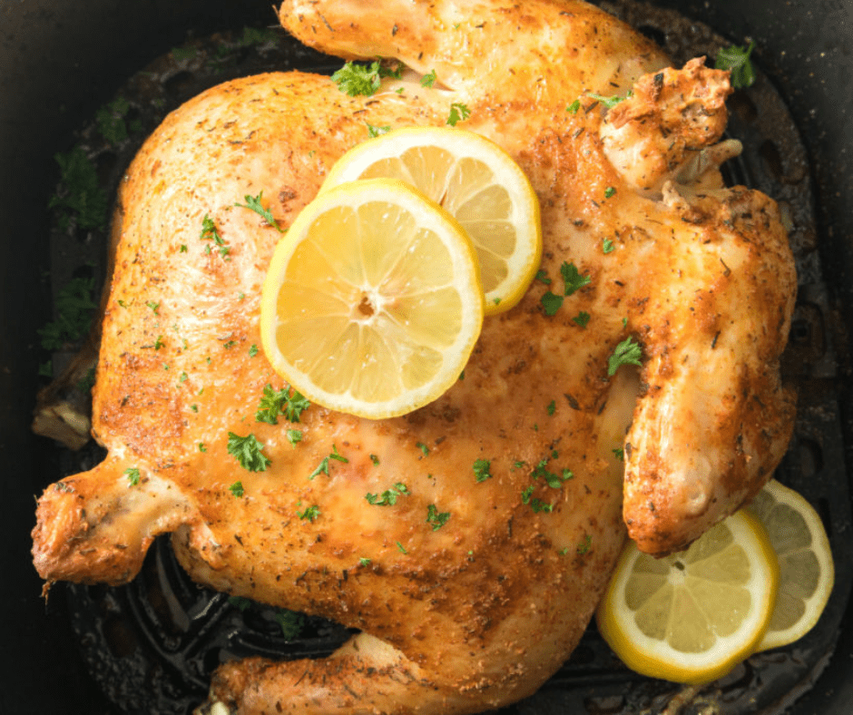 An aerial view of an air fryer rotisserie chicken with two slices of lemon on top with herbs and two slices of lemon on the side.