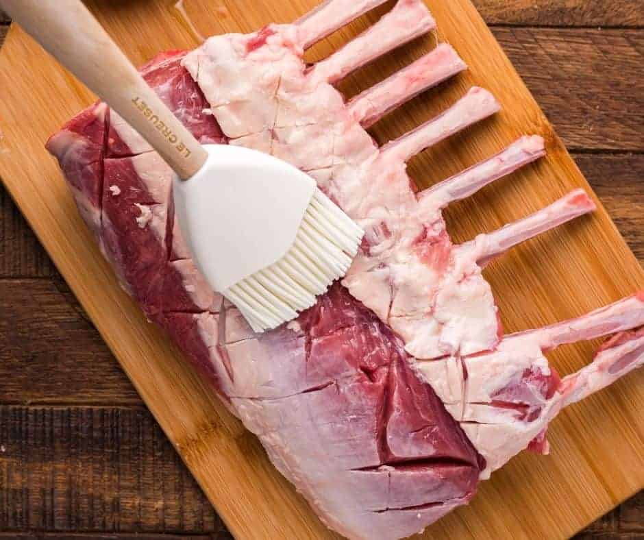 Raw air fryer rack of lamb on a wooden cutting board with rubber brush