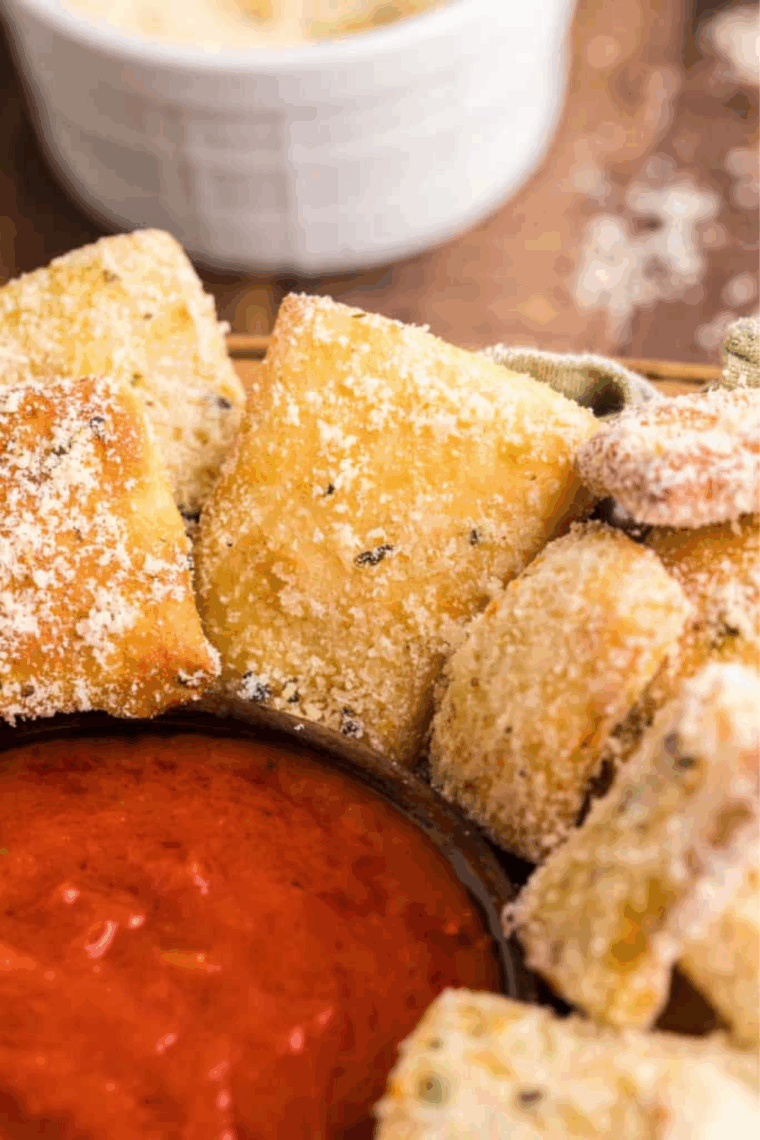 A pile of small, golden-brown homemade Domino's style garlic bread knots, heavily brushed with garlic butter and topped with Parmesan cheese and dried herbs.