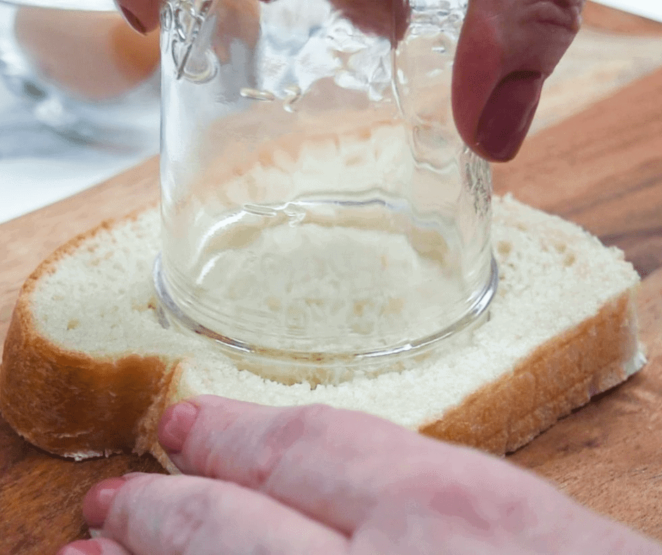 Someone using a glass jar to cut a circle into a slice of bread to make this egg in toast hole recipe.