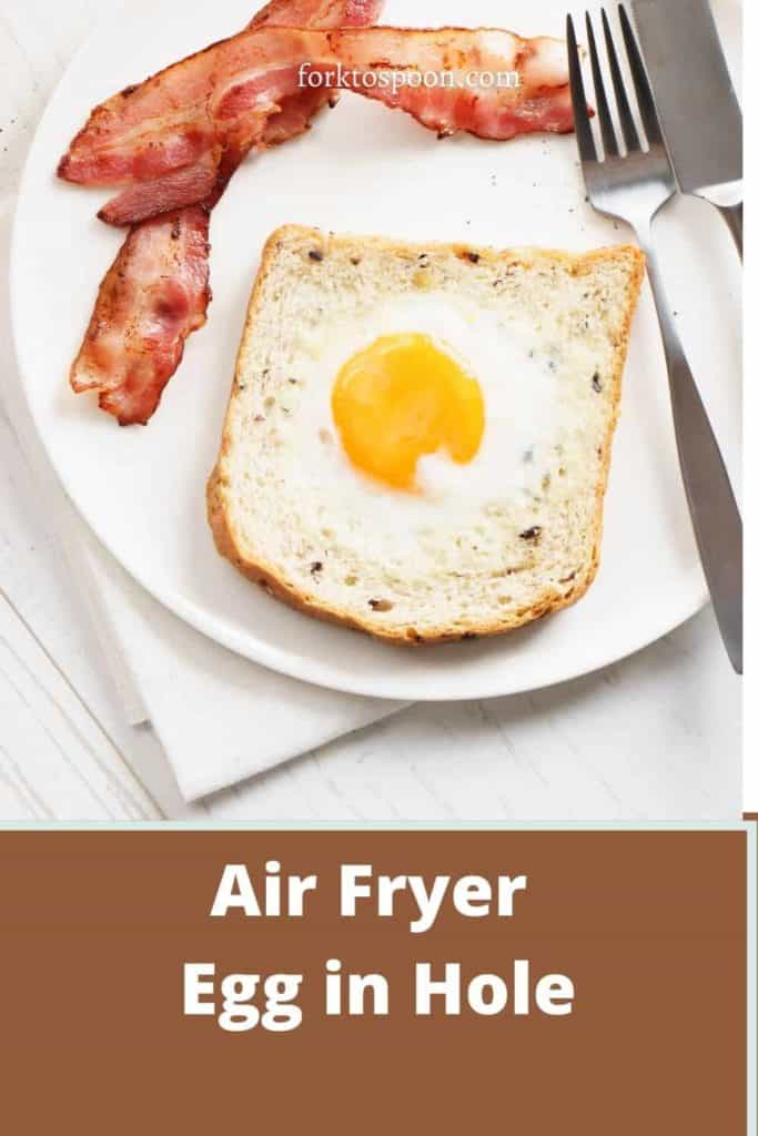 An aerial view of egg in bread hole on a white plate with two slices of bacon and a fork and knife. Text reads "Air Fryer Egg in Hole."