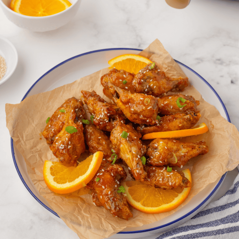 Plate of golden, crispy gluten-free chicken wings served with dipping sauce and garnished with fresh herbs.