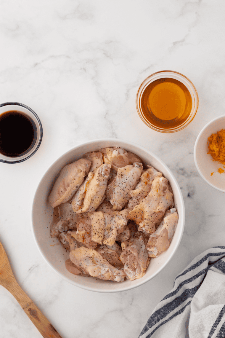Raw chicken wings on a plate being patted dry with paper towels.