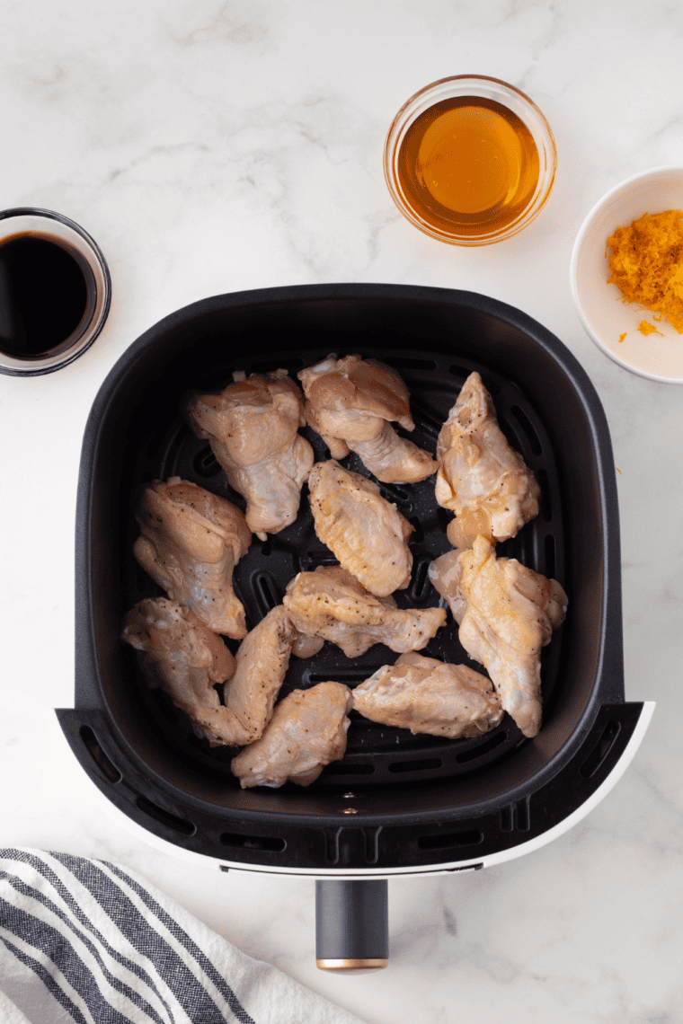 Chicken wings cooking in a single layer inside an air fryer basket.