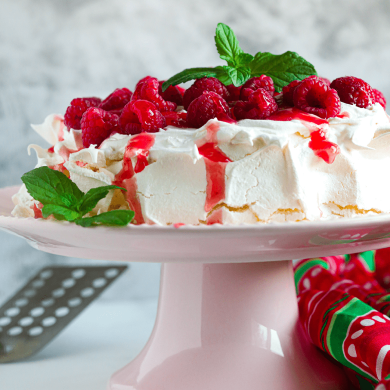 side view: raspberry pavlova on a pink cake stand with fresh berries and mint on top