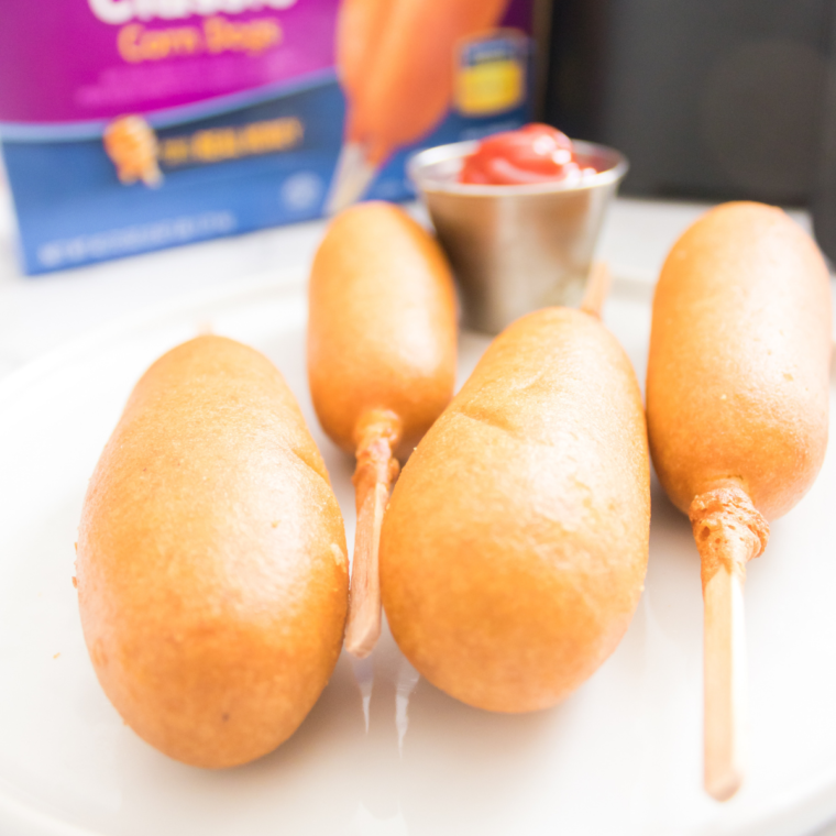 Golden, crispy State Fair-style corn dogs cooked in an air fryer, served with dipping sauces on a plate.