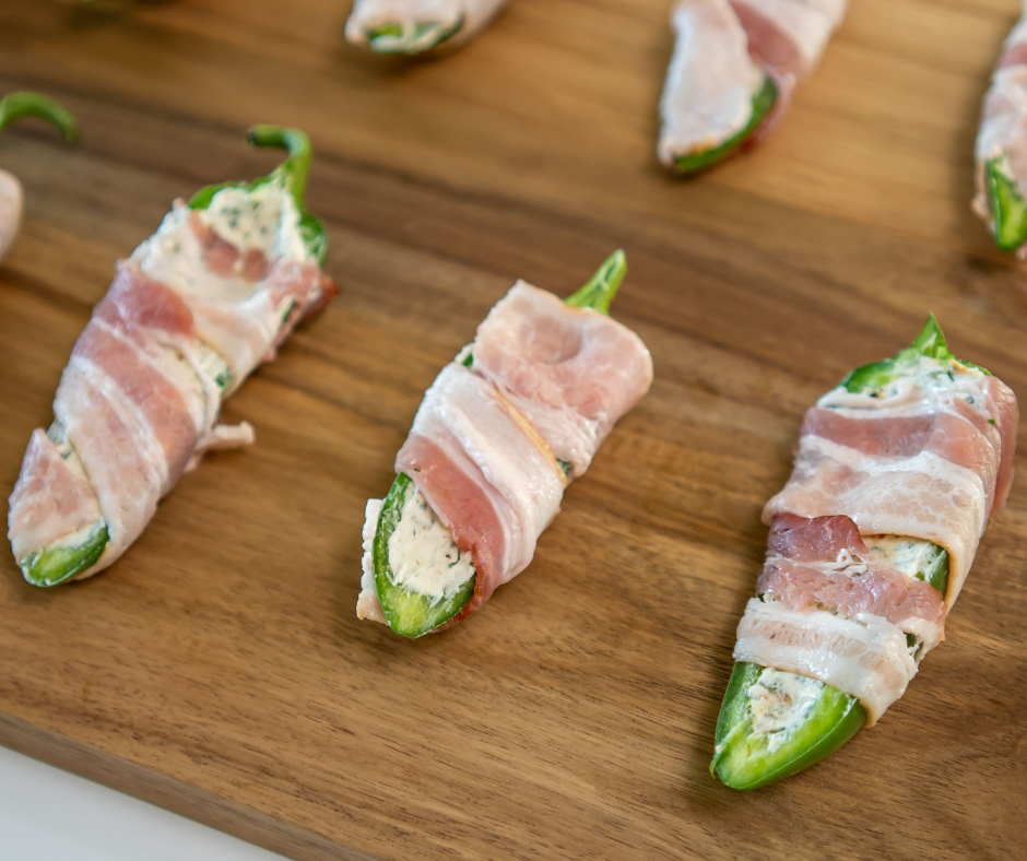 Bacon wrapped stuffed jalapenos on a wooden cutting board.