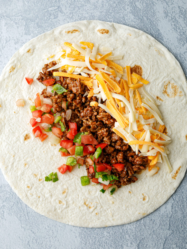 In a skillet over medium-high heat, brown and crumble ground beef. Drain excess grease.

Lay out 4 flour tortillas and spoon an equal amount of the ground beef mixture across the center of each.
Place an equal amount of cheese and an equal amount of fresh salsa on either side of the ground beef.
Roll the tortillas up and over the ingredients, tucking the sides in as you go to create burritos.