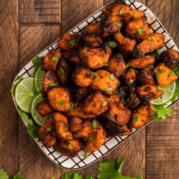 Air Fryer BBQ Chicken Bites served on a plate, garnished with fresh herbs, showcasing crispy, golden pieces of chicken coated in barbecue sauce.