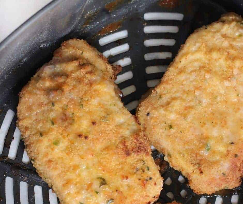 Close up Air Fryer Breaded Pork Chops in the air fryer basket while cooking. They are golden brown in color with a crispy looking outside. 
