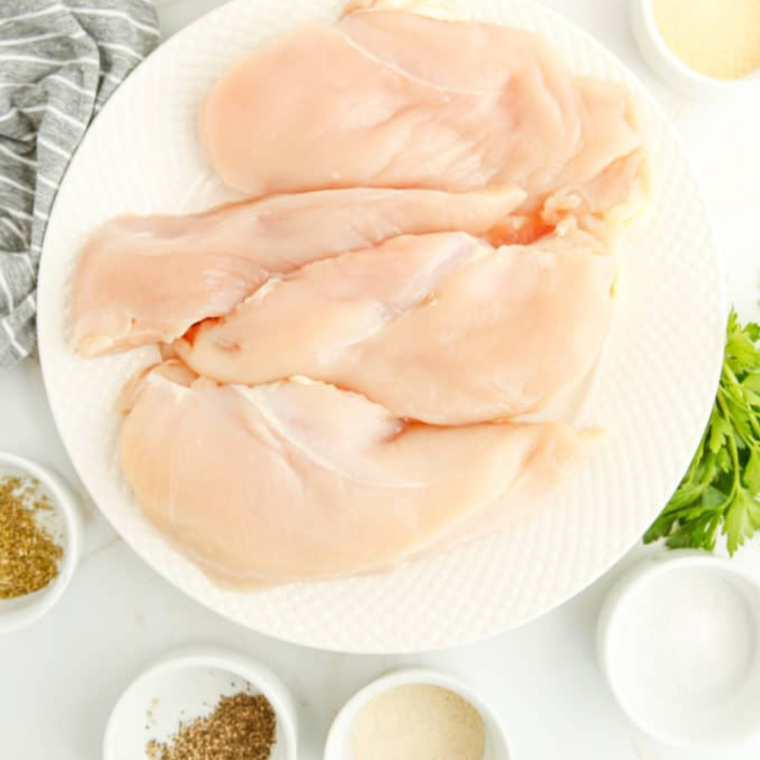 Butterflying a chicken breast on a cutting board with a sharp knife, trimming excess fat and tendons