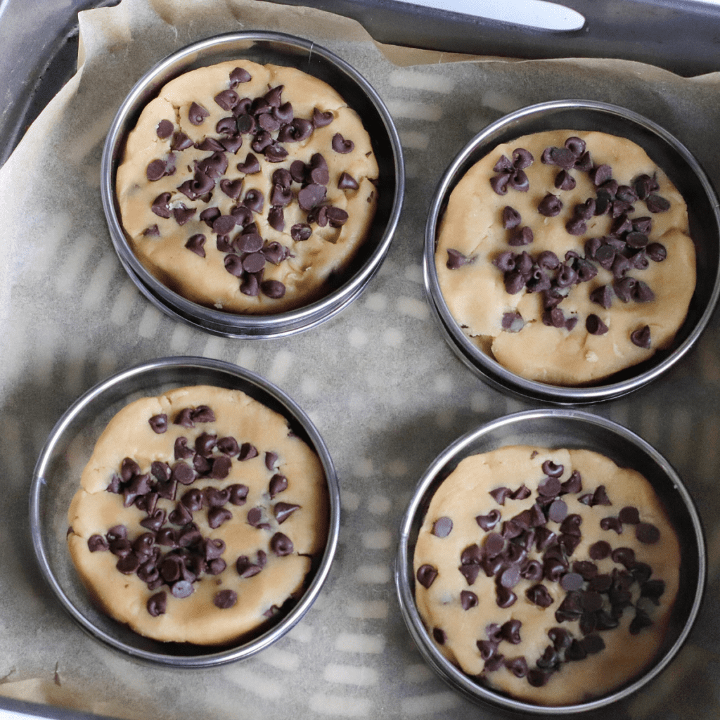 Thick, golden-brown cookies cooling in muffin rings, with soft centers, resting for ten minutes before transferring to a cooling rack.