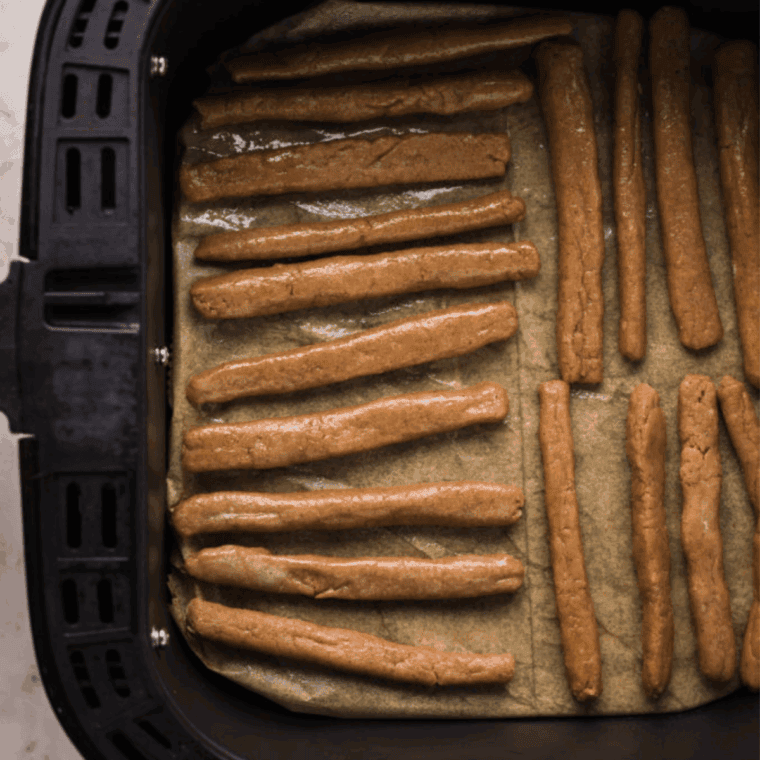 Arranging funnel cake fries in an air fryer basket, spraying with oil, cooking, then dusting with powdered sugar and serving with dip.