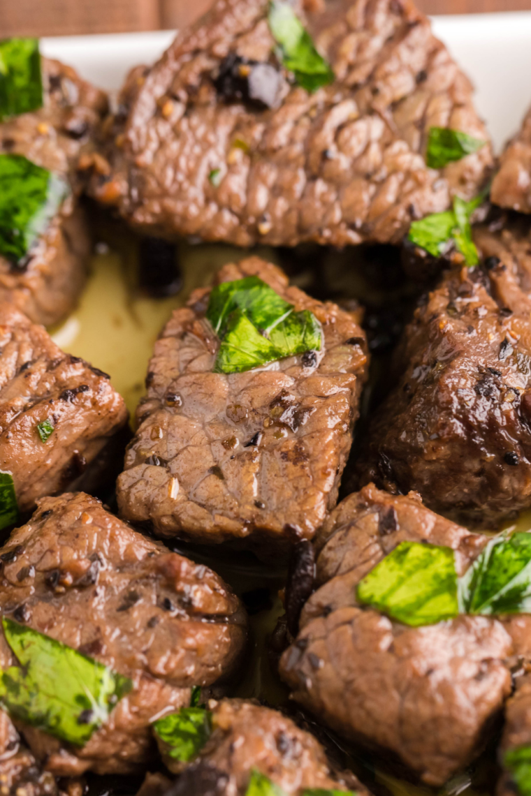 Garlic butter steak bites resting on a plate, finished with flaky salt, black pepper, and fresh parsley garnish.