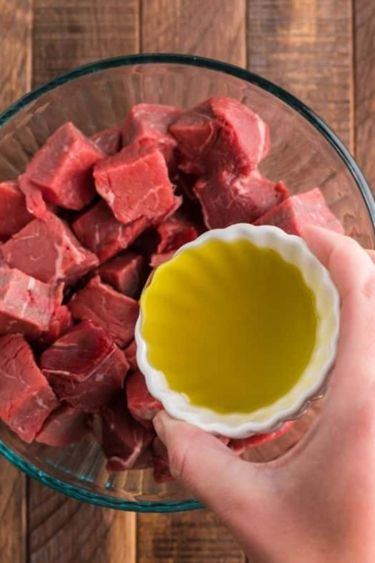 Steak cubes tossed in a bowl with oil and seasonings, evenly coated for bold flavor before air frying.