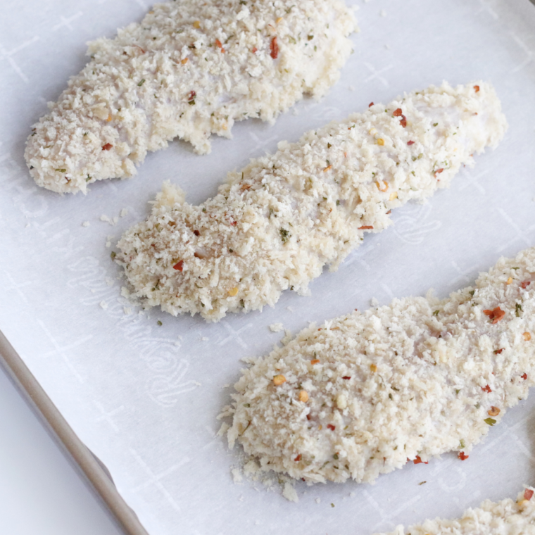 Placing the chicken fingers onto a baking sheet with parchment paper.