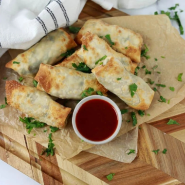 Air fryer chicken cilantro egg rolls stacked on a platter with lime wedges and dipping sauce